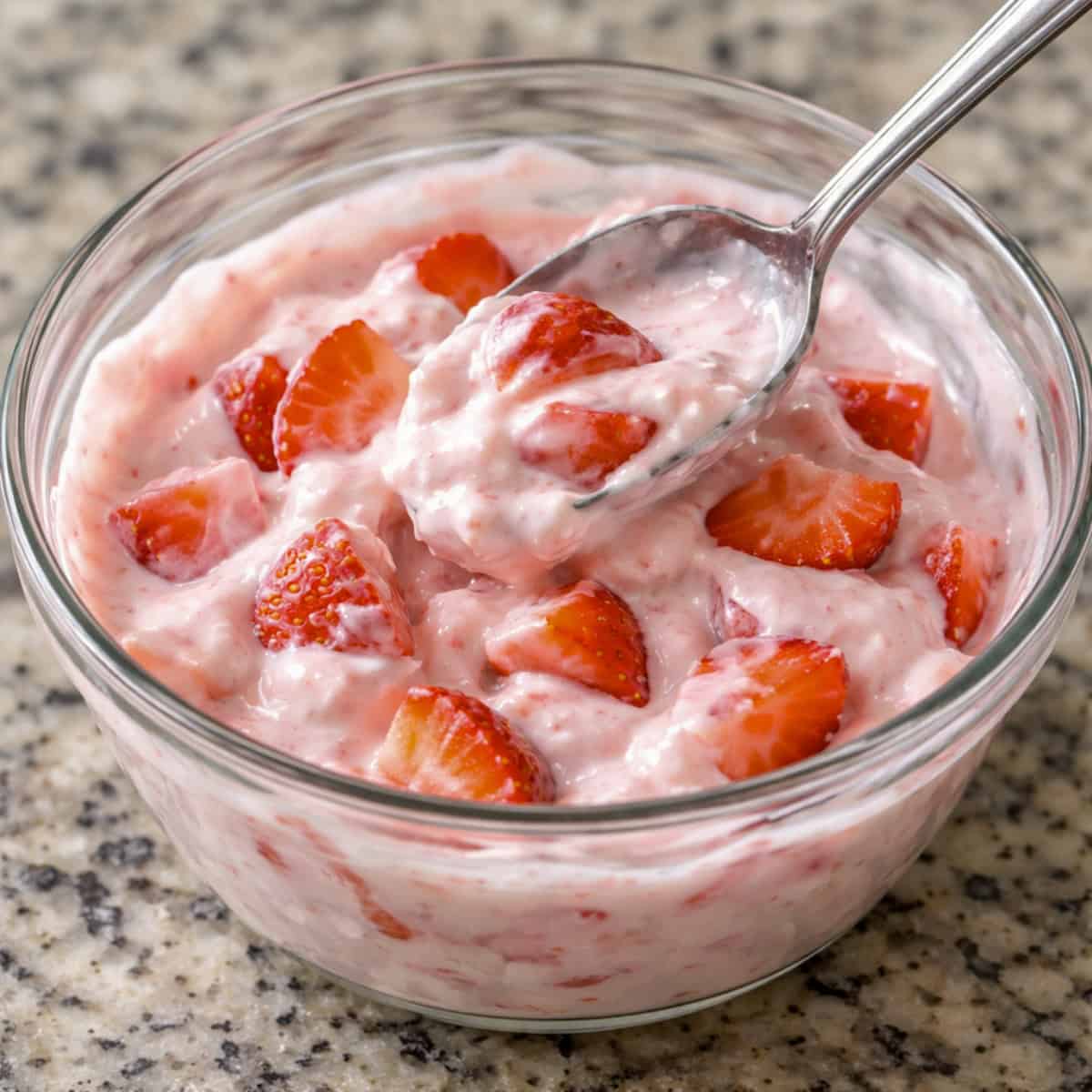 Mixing strawberries, yogurt and lite whipped topping in glass bowl with spoon.
