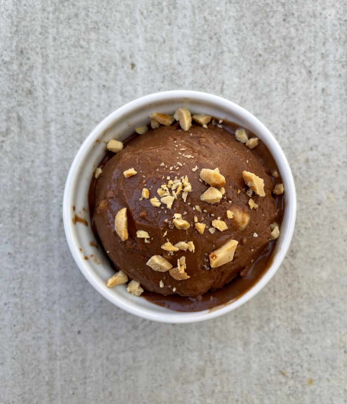 Peanut butter chocolate nice cream in white dish topped with chopped peanuts.