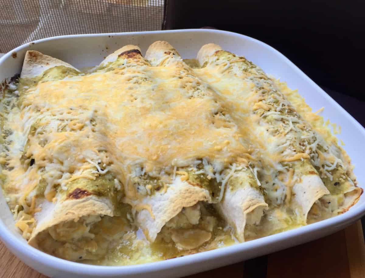Fresh baked chicken enchiladas verde topped with melted cheese in baking dish.