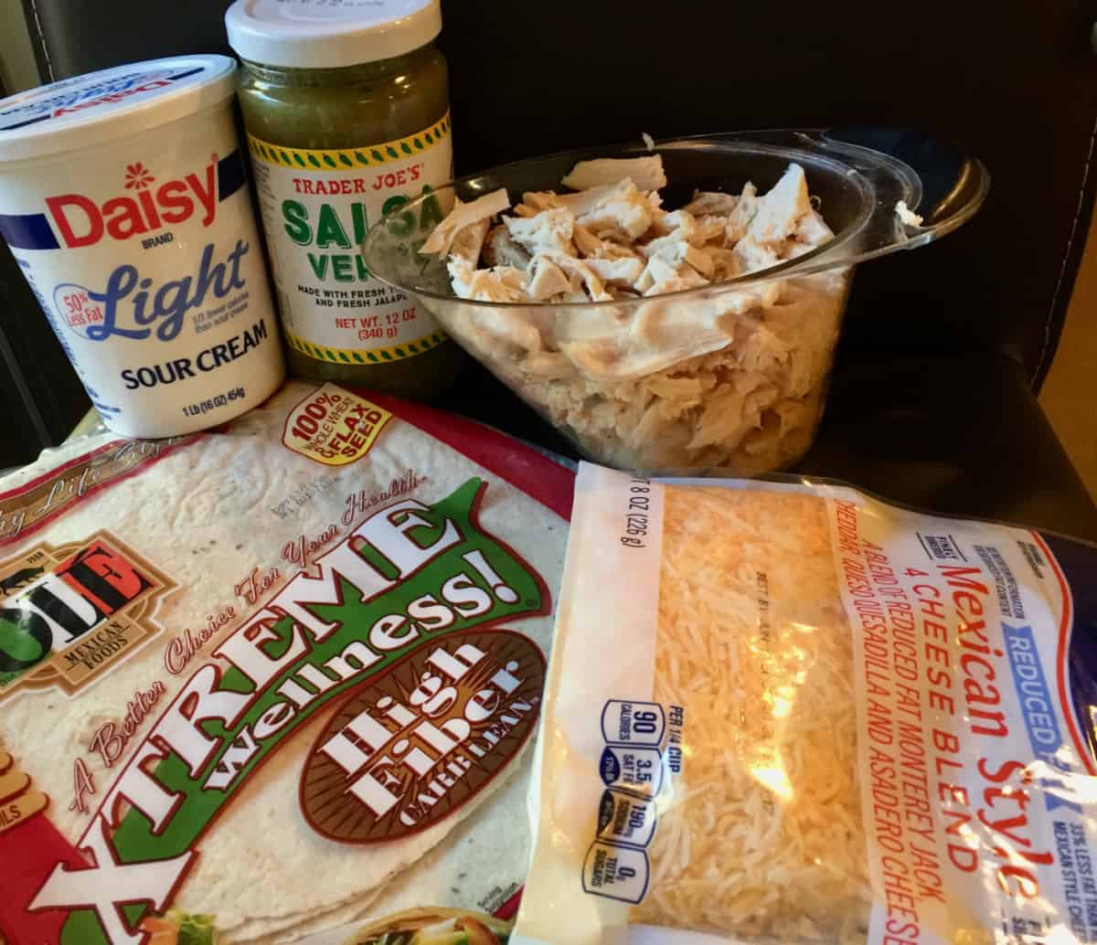 Ingredients for making enchiladas verde including low carb tortillas, cooked chicken, shredded cheese, salsa verde and light sour cream.