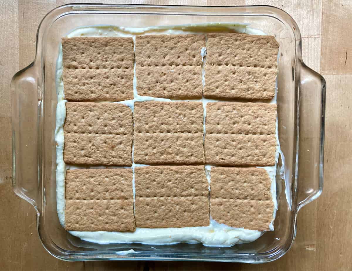 Adding layer of graham crackers on top of pudding mixture in glass dish.