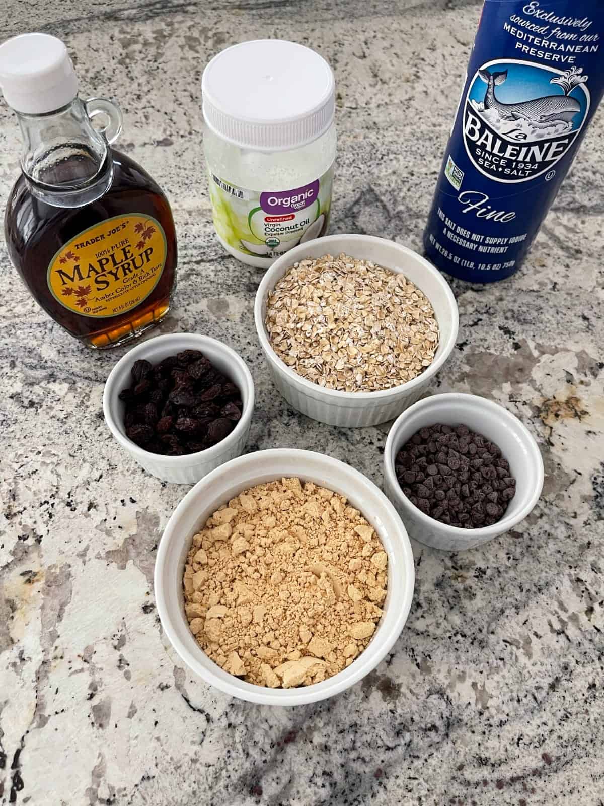 Ingredients including maple syrup, coconut oil, sea salt, oats, raisins, mini chocolate chips and powdered peanut butter.