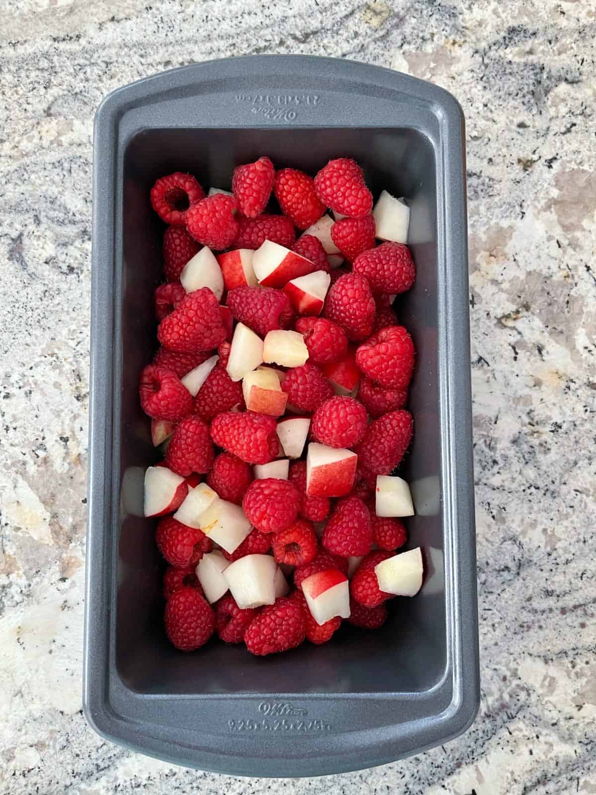 Chopped nectarines and raspberries in loaf pan.