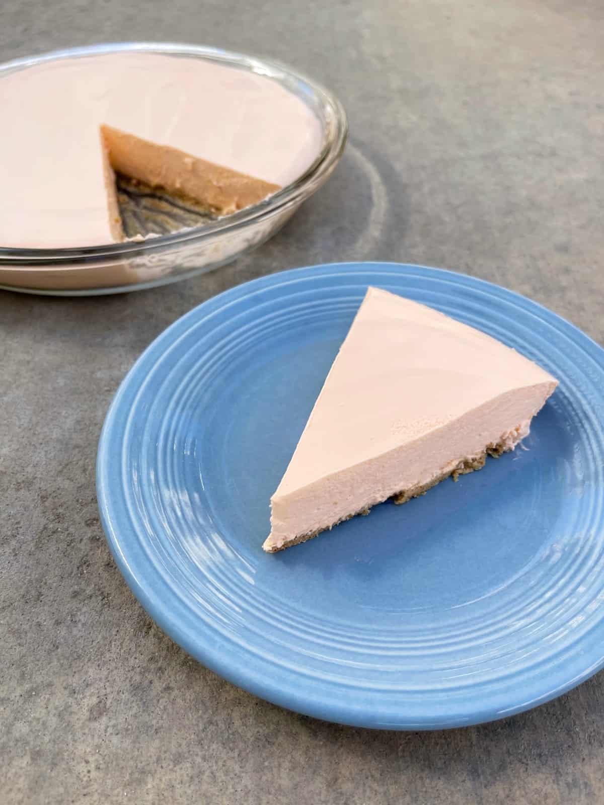 Creamy orange creamsicle no-bake pie piece on blue plate with pie dish in background.