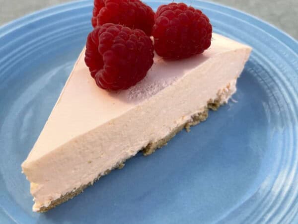 slice of no bake orange creamsicle pie topped with fresh raspberries on blue fiesta ware plate from above