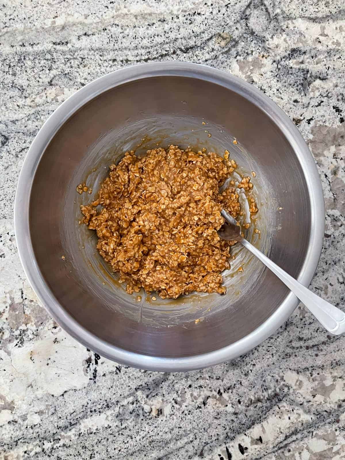 Combining peanut butter granola bar batter in mixing bowl with fork.
