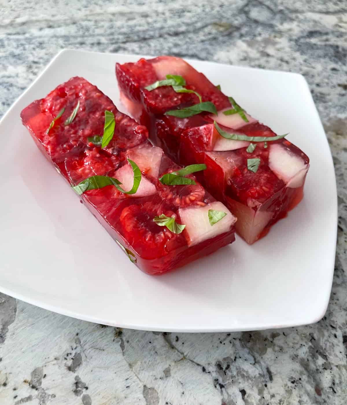 Two slices raspberry nectarine Jello terrine topped with fresh mint on small white plate.