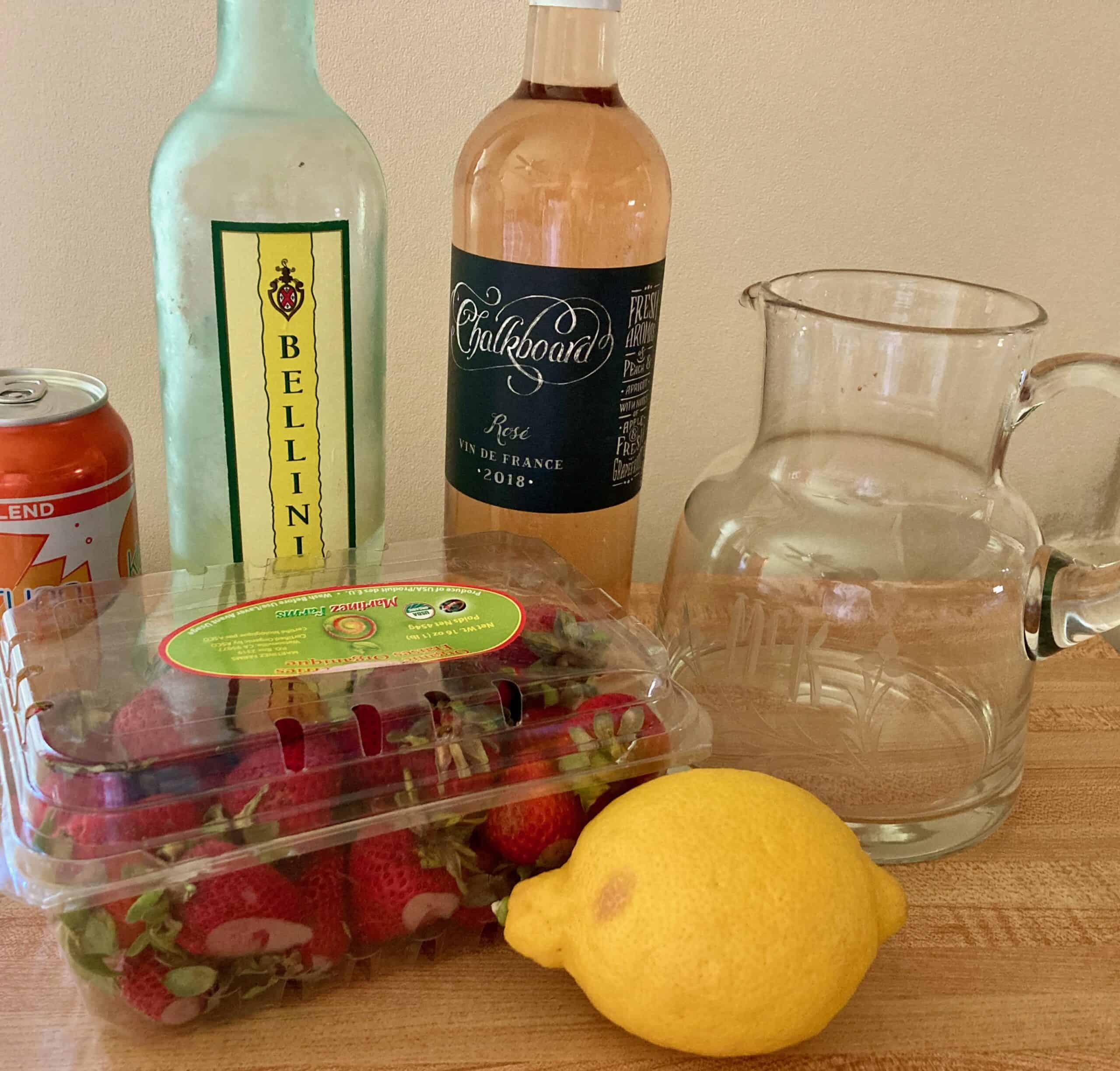 Bottle of rose wine, Limoncello, seltzer, fresh strawberries, lemon and glass pitcher.