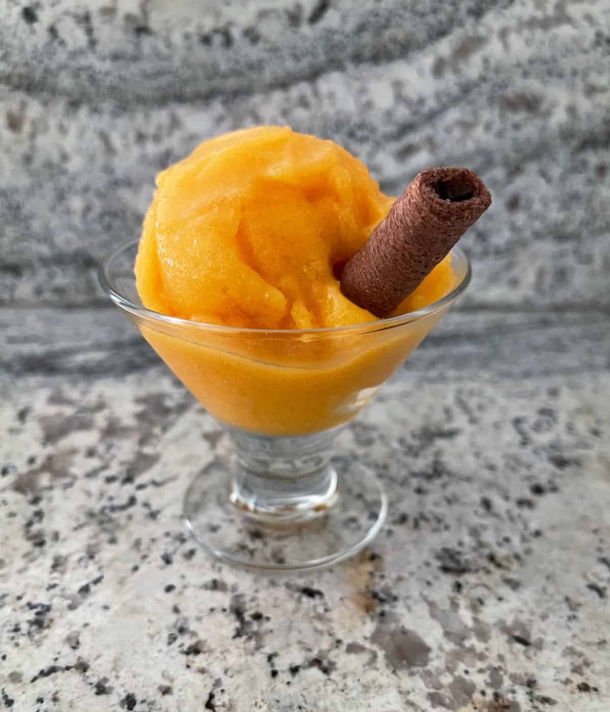 Fat-free apricot sorbet in glass dish with chocolate coconut roll wafer cookie.