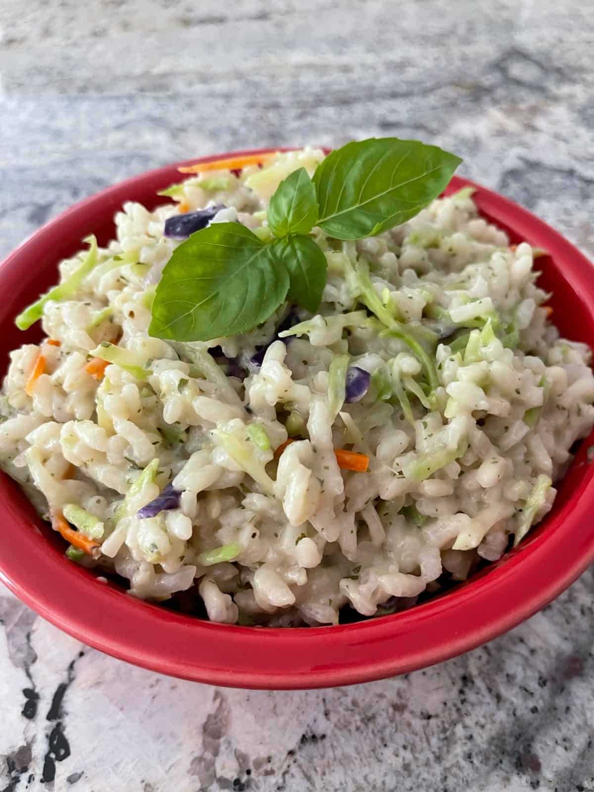 Creamy broccoli slaw risotto topped with fresh basil in red serving bowl.