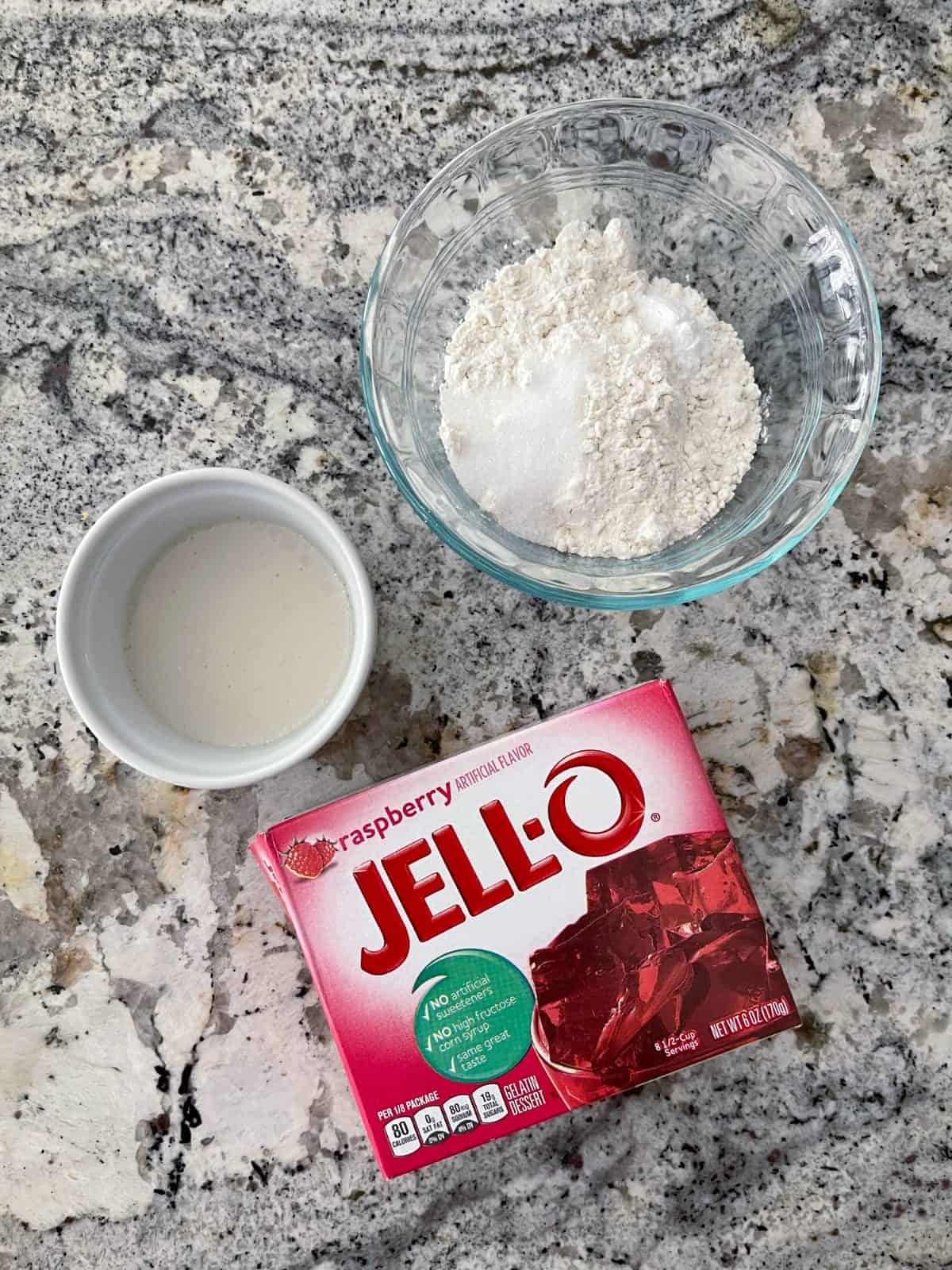 Συστατικά που περιλαμβάνουν γάλα αμυγδάλου χωρίς ζάχαρη, αλεύρι για όλες τις χρήσεις, γλυκαντικό Swerve και συσκευασία Jell-o βατόμουρου.