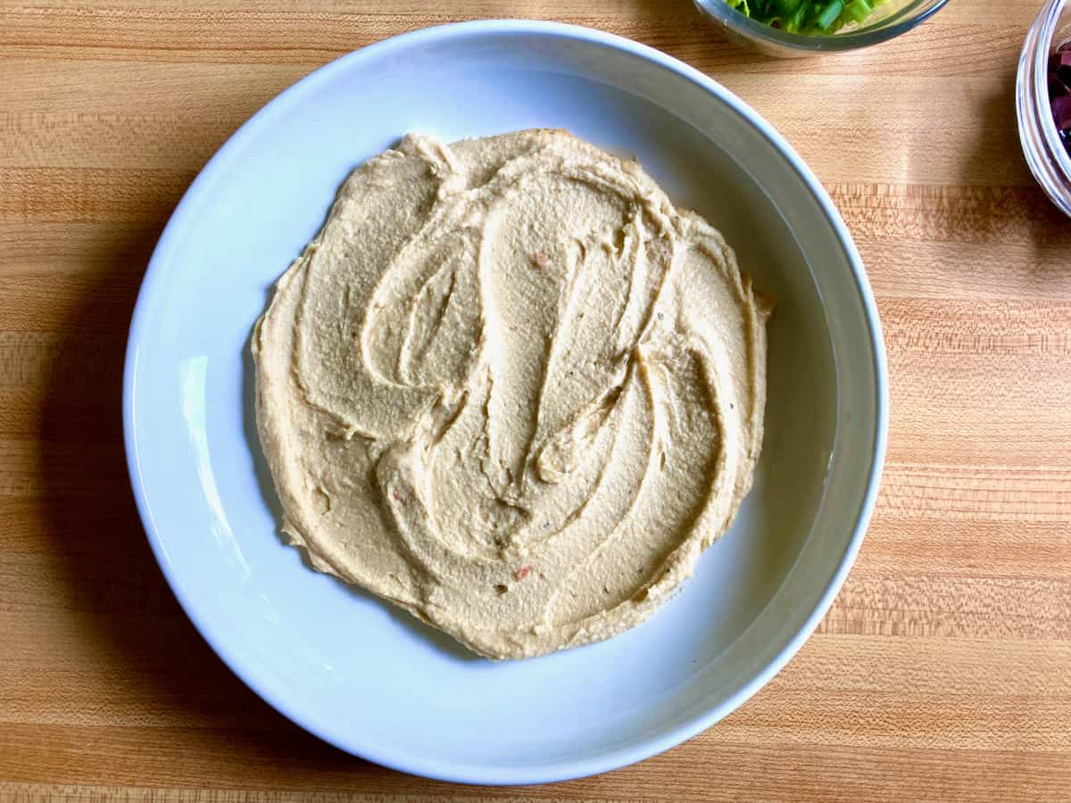 Hummus spread on white plate for making Greek dip.
