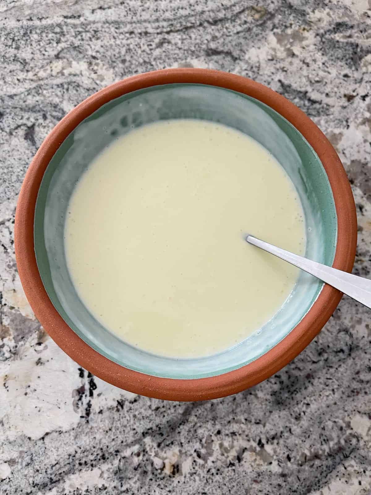 Mixing lemon jello with vanilla yogurt with spoon in green bowl.