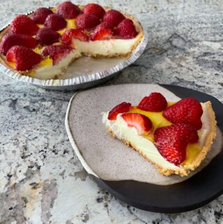 slice of no bake strawberry lemon pie on pottery plate with full pie in the background
