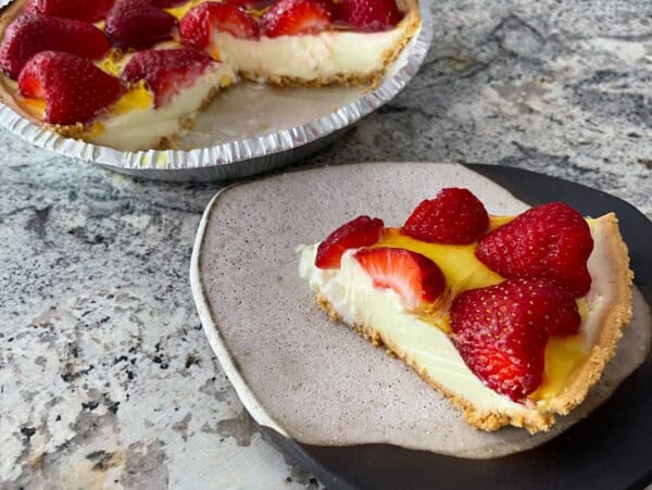 slice of no bake strawberry lemon pie on pottery plate with full pie in the background