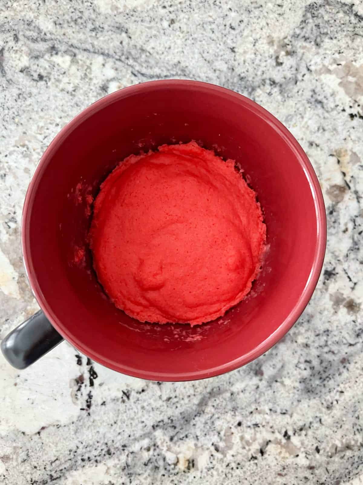 Fresh cooked raspberry Jell-o microwave cake in red mug on granite counter.