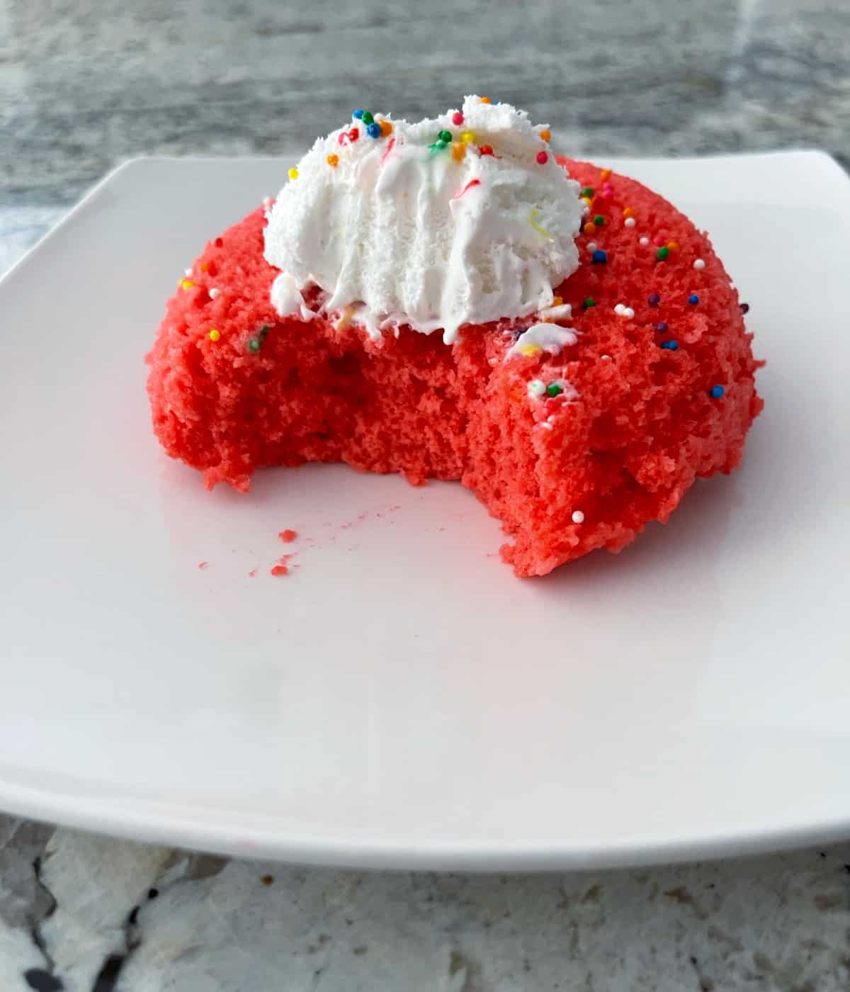 Single serving Raspberry Jello Mug Cake with sprinkled and whipped topping on white plate.