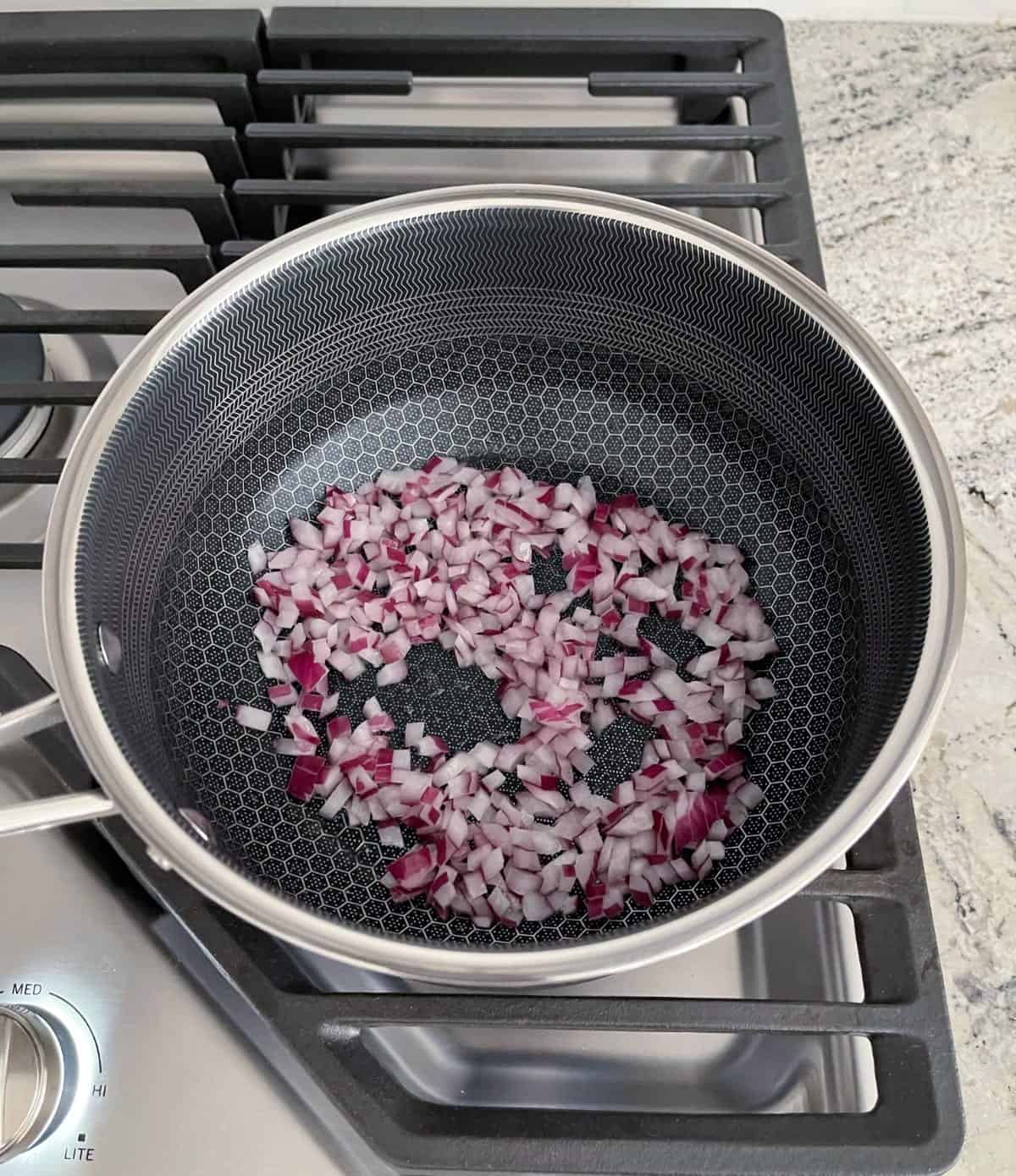 Sauteeing chopped red onion in saucepan on stovetop.