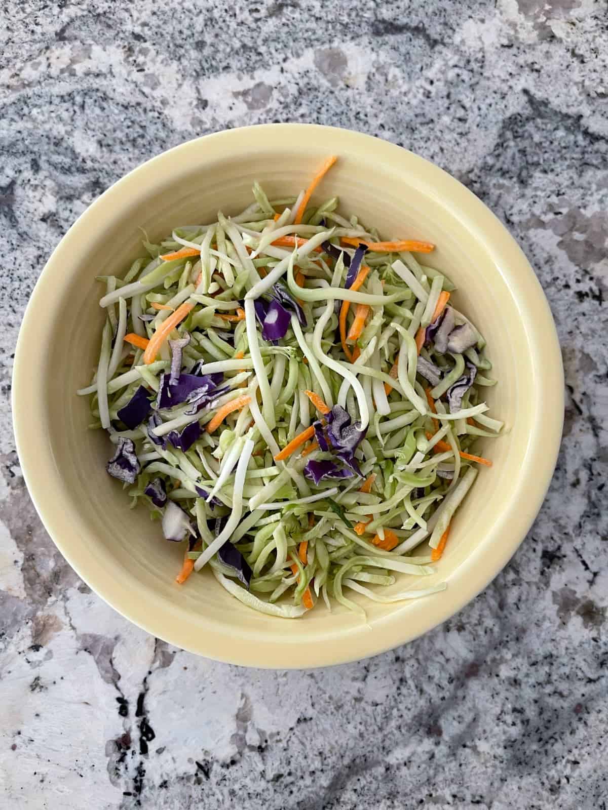 Packaged broccoli slaw coleslaw mix in yellow bowl.