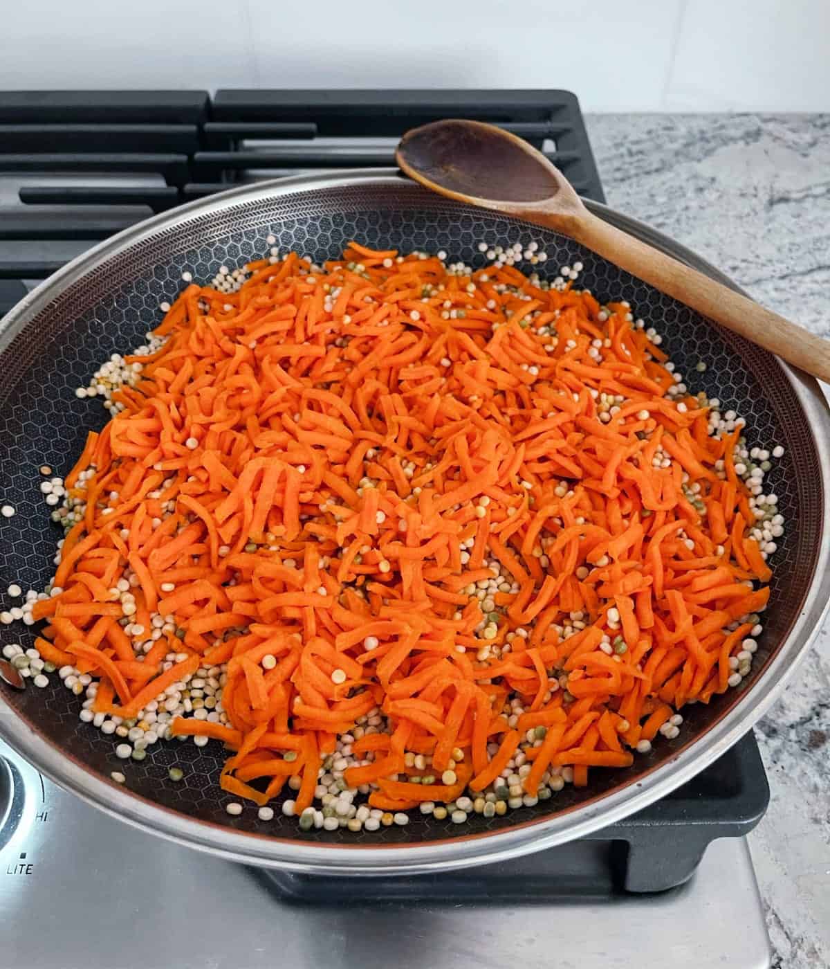 Sauteing shredded carrots and Israeli couscous in skillet.