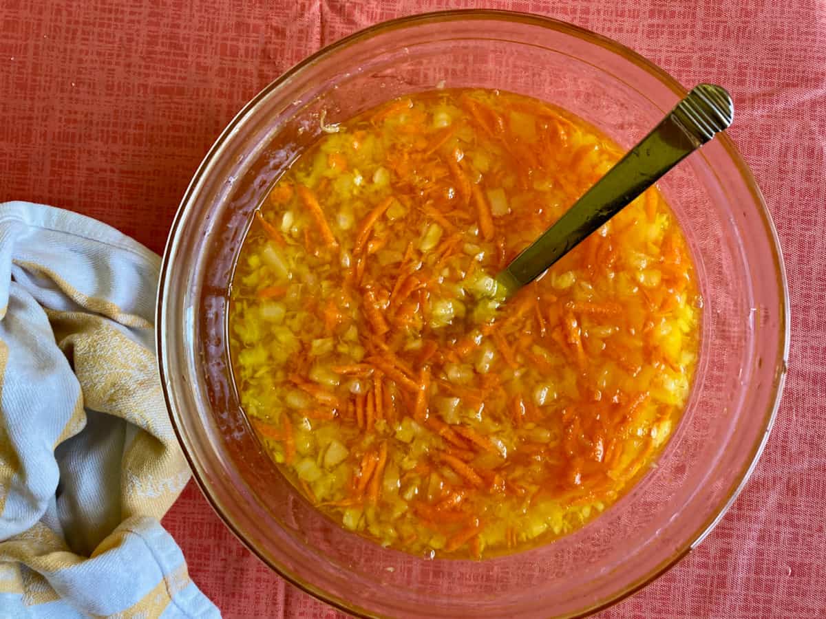 Mixing gelatin with crushed pineapple and shredded carrot in glass mixing bowl.