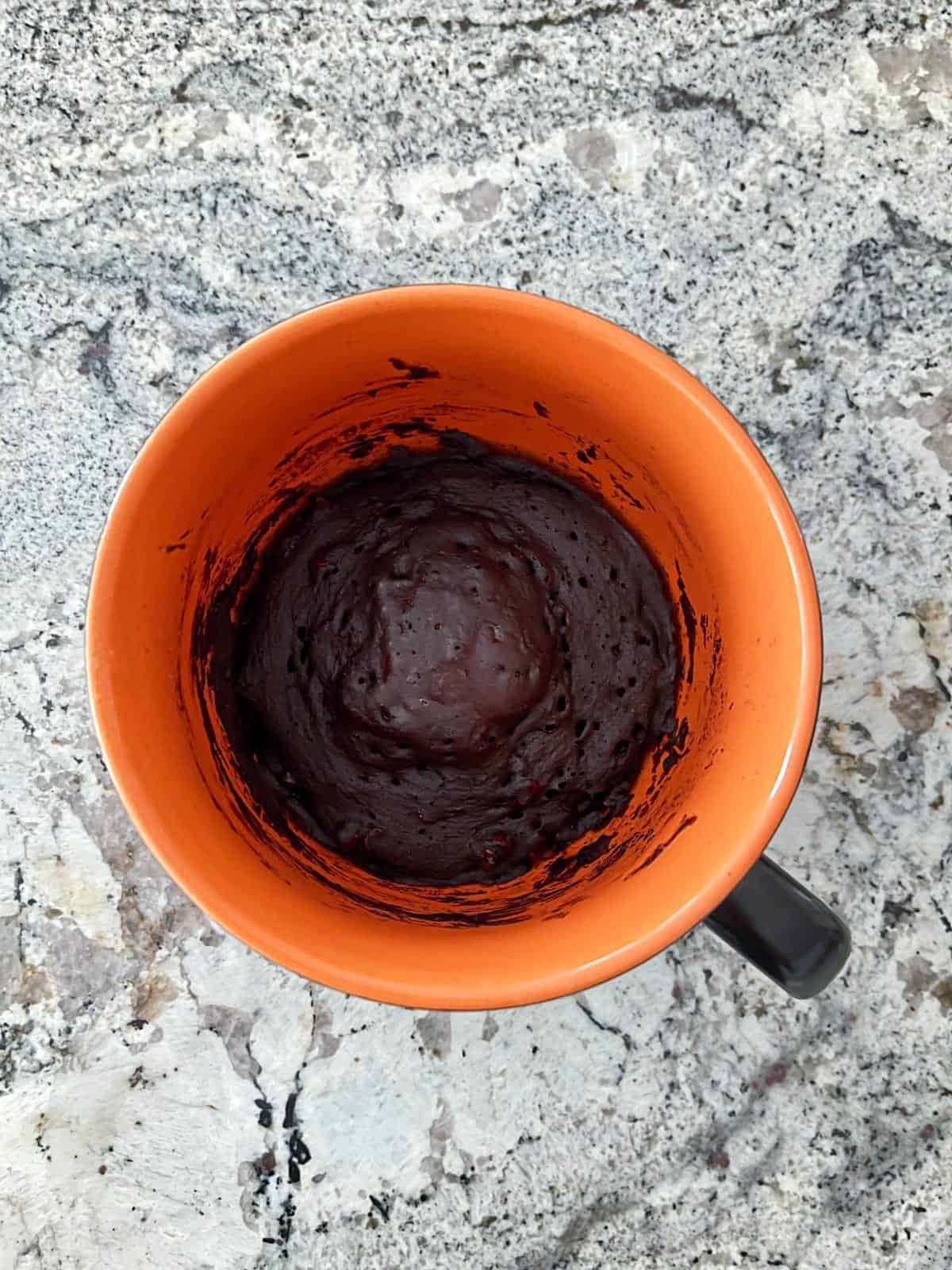 Microwave Black Forest Chocolate Cake in orange mug on granite counter.