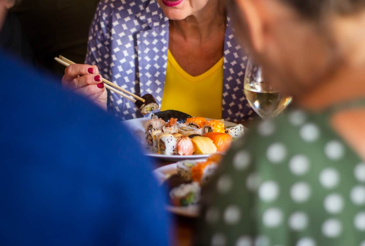 Woman eating sushi with chopsticks at table close up.