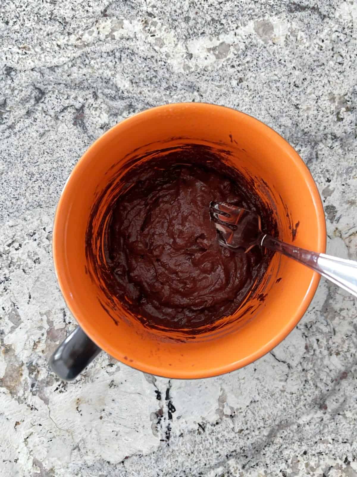 Folding chocolate chips into Black Forest Chocolate Cake batter in orange mug with fork.
