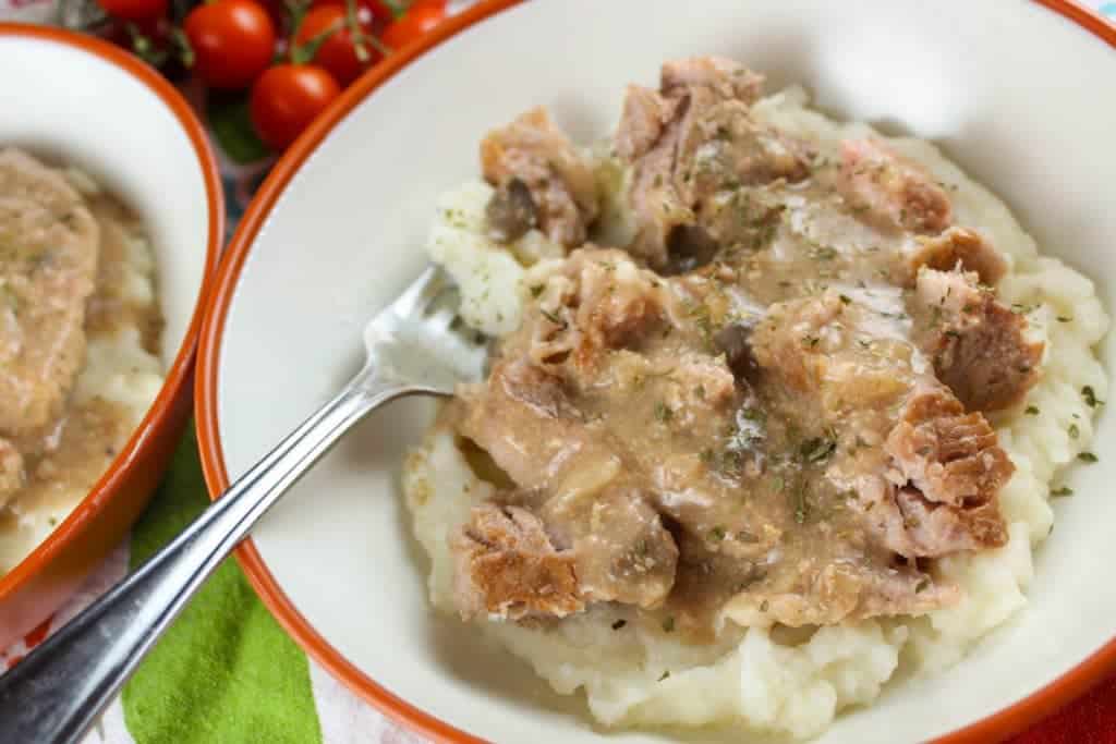 Crock Pot Pork Chops in Creamy Gravy Over Mashed Potatoes in a Bowl