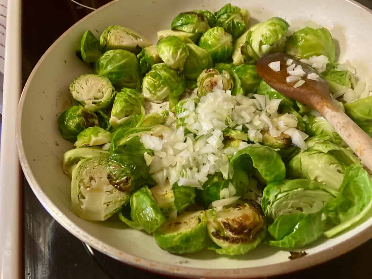 Adding chopped onion and water to skillet of brussels sprouts.