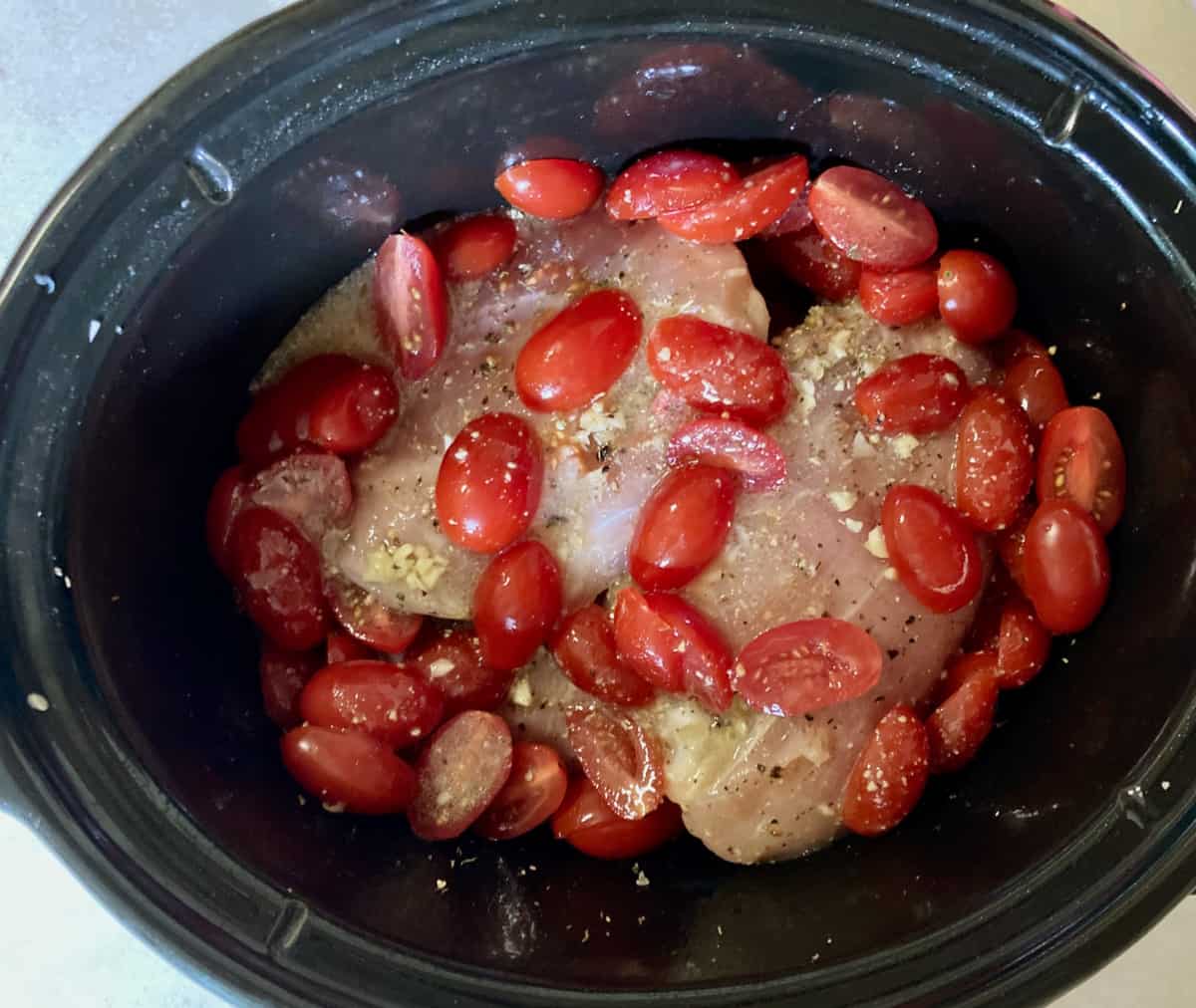 Seasoned chicken breasts topped with tomatoes and broth in black crock pot.