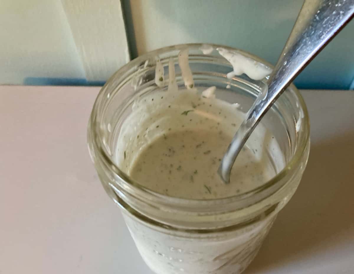 Homemade skinny ranch dressing in jar with spoon.