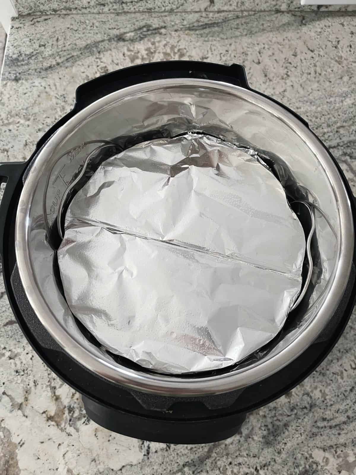 Aluminum foil covered mini bundt pan on wire steam rack in Instant Pot.