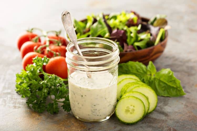 Cucumber slices and bowl of mixed greens with jar of homemade ranch dressing.