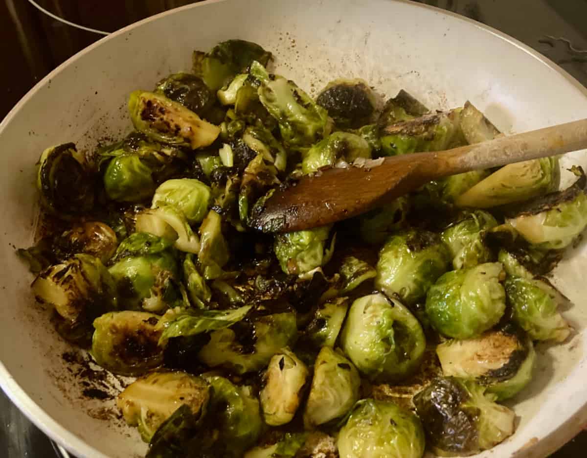 Cooked Brussels sprouts in skillet with wooden spoon.