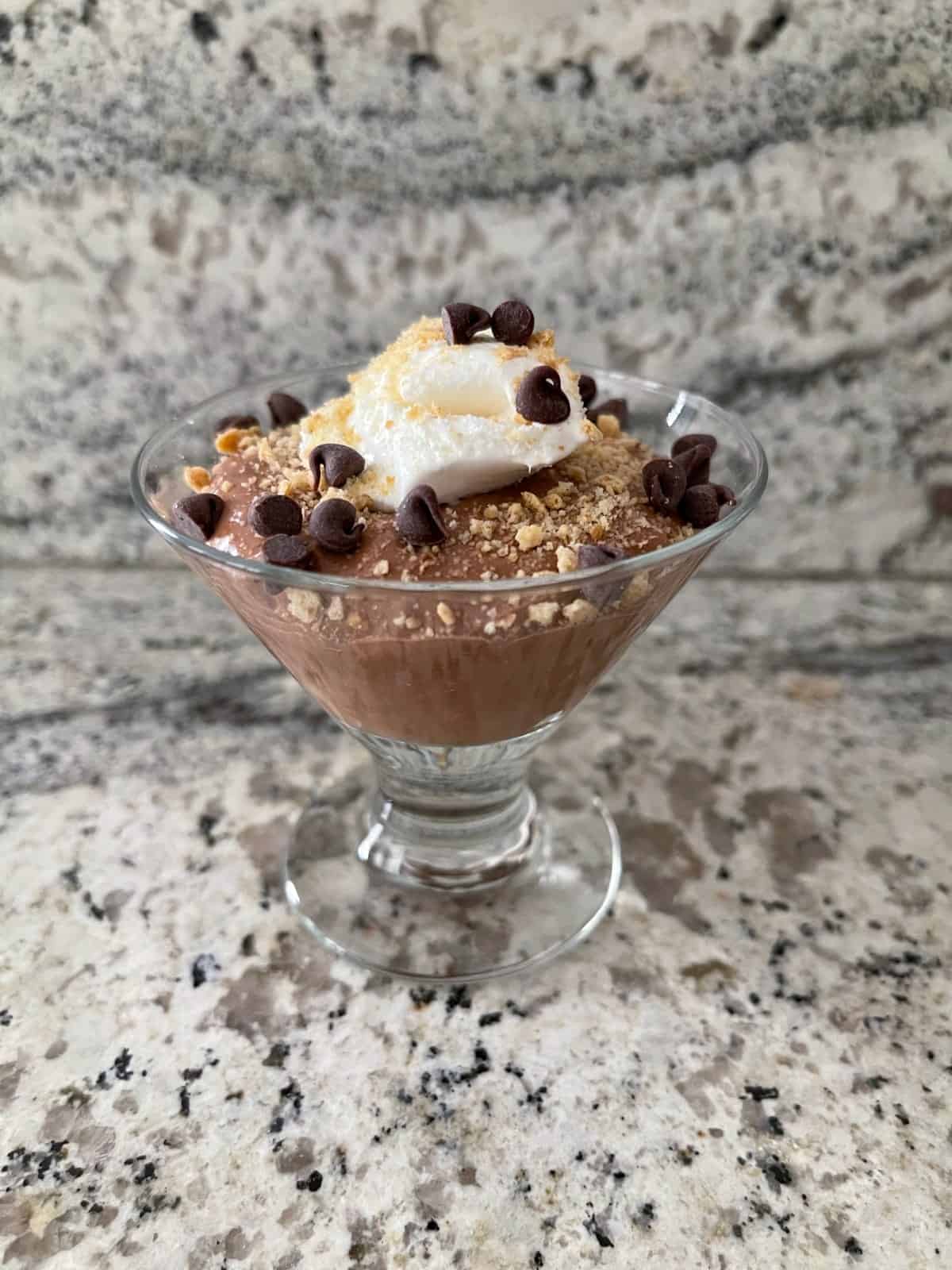 Spoonable chocolate cheesecake dessert cup topped with whipped topping, graham cracker crumbs and mini chocolate chips.