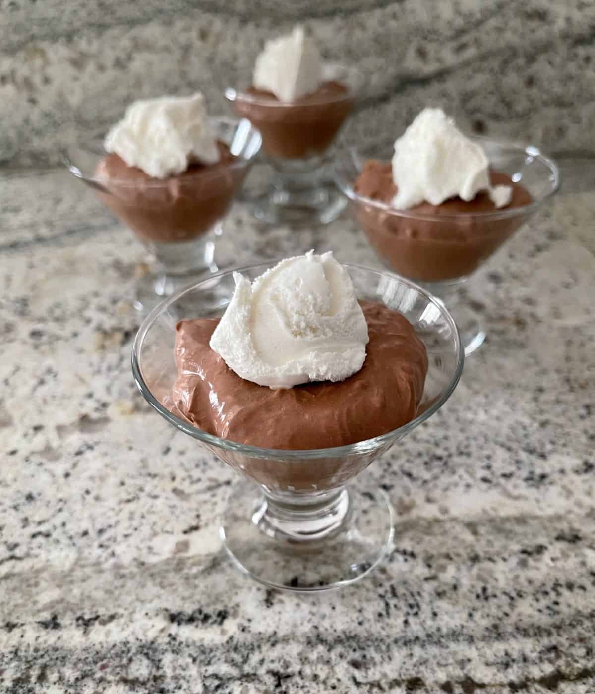 Four dessert glasses with spoonable chocolate cheesecake topped with light whipped topping.