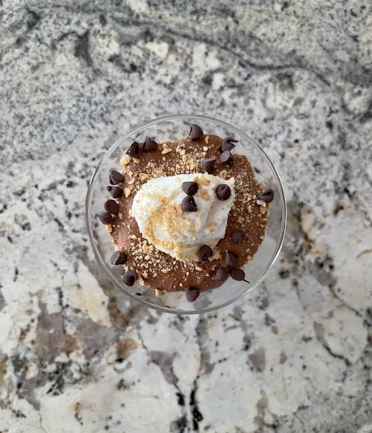 Looking down on chocolate cheesecake dessert cup garnished with whipped topping, graham cracker crumbs and mini chocolate chips.