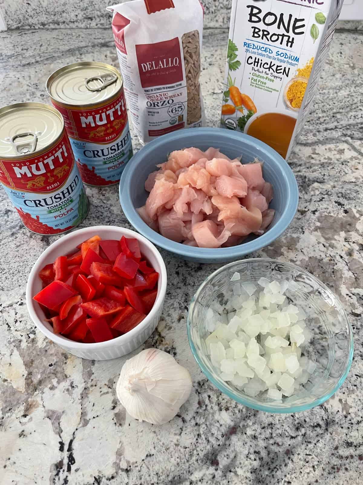Ingredients including canned crushed tomatoes, whole wheat orzo, chicken broth, chopped chicken breasts, chopped onion, chopped red bell pepper and garlic clove.