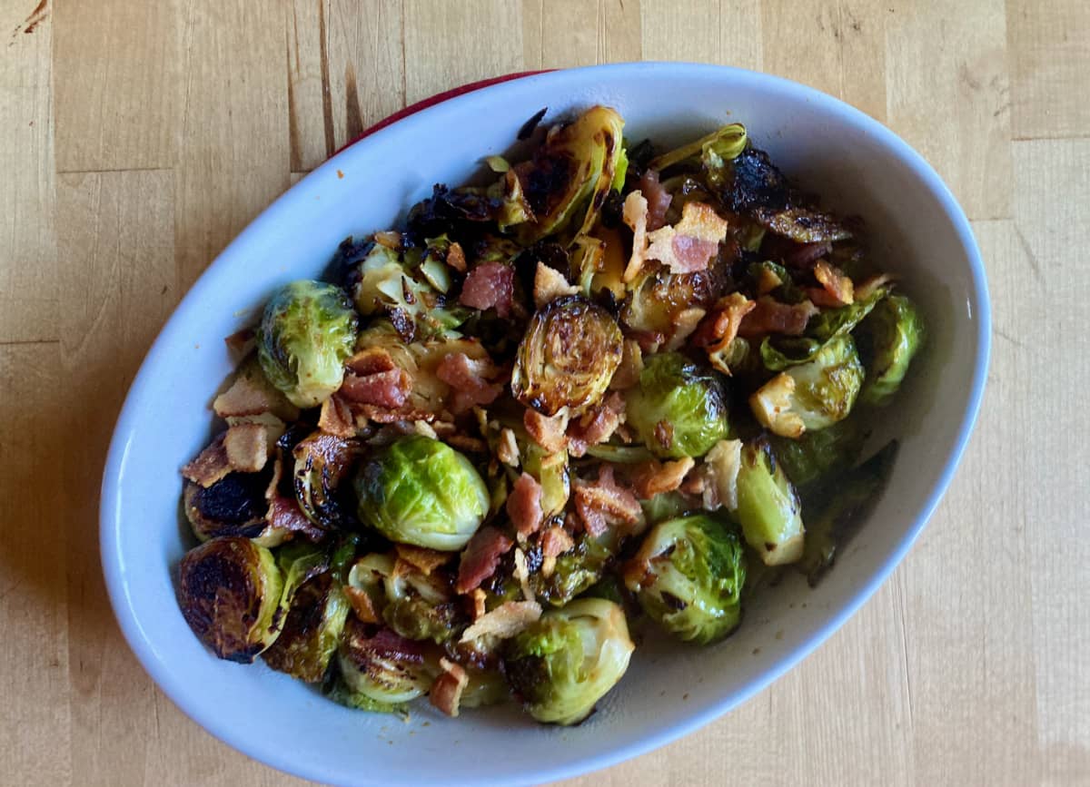 Skillet roasted Brussels sprouts with crumbled bacon oval white dish.
