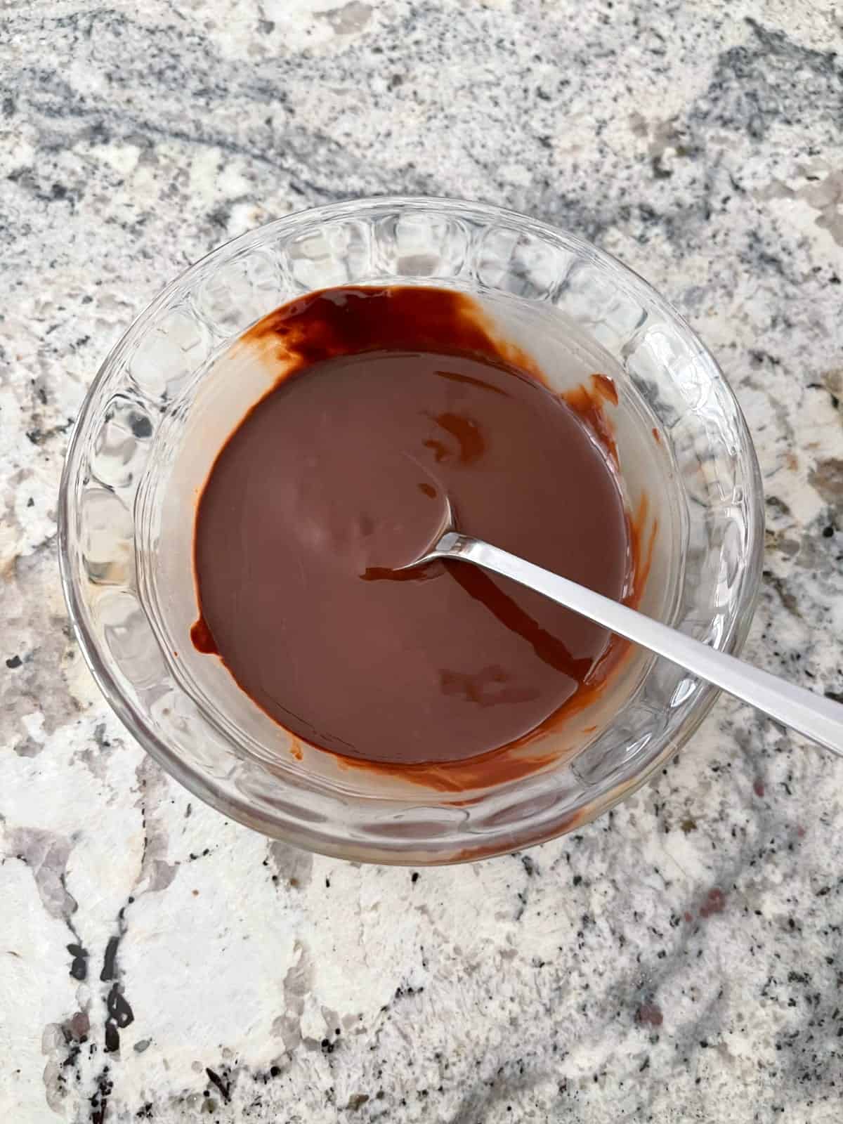 Stirring melted chocolate with spoon in small glass bowl.