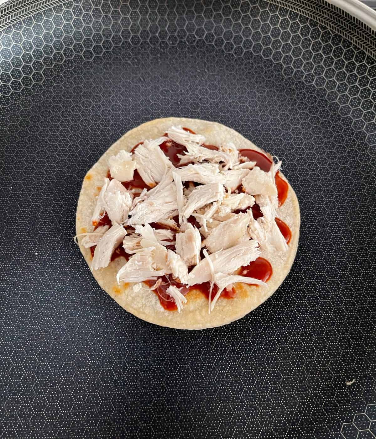 Cooking Mexican pizza with chicken in skillet.