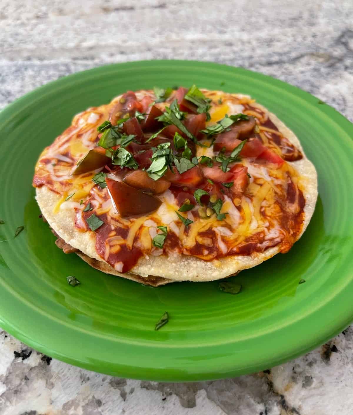 Homemade Mexican Pizza topped with chopped cilantro on green plate.