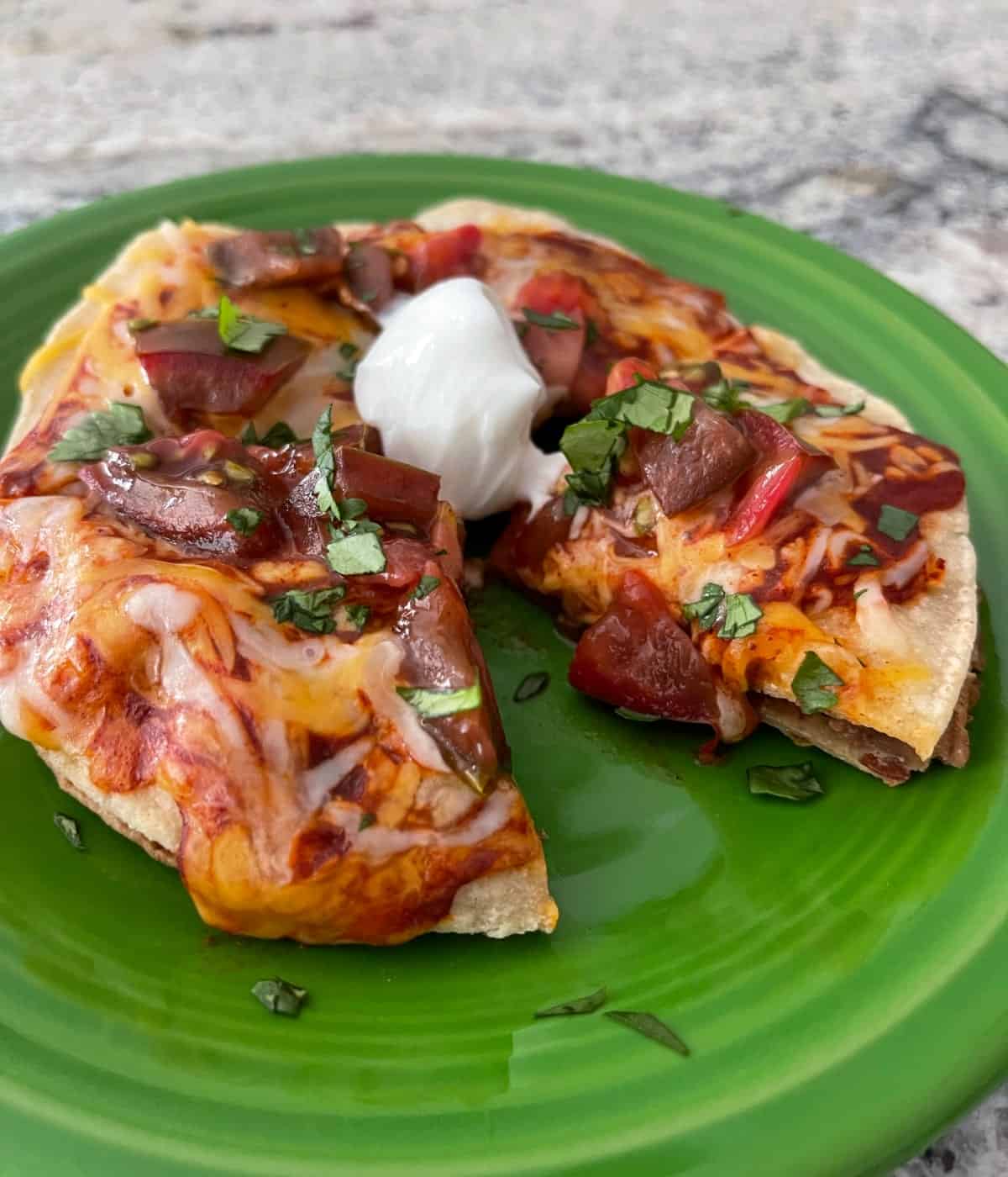 Skillet Mexican pizza garnished with chopped cilantro and sour cream on small green plate.