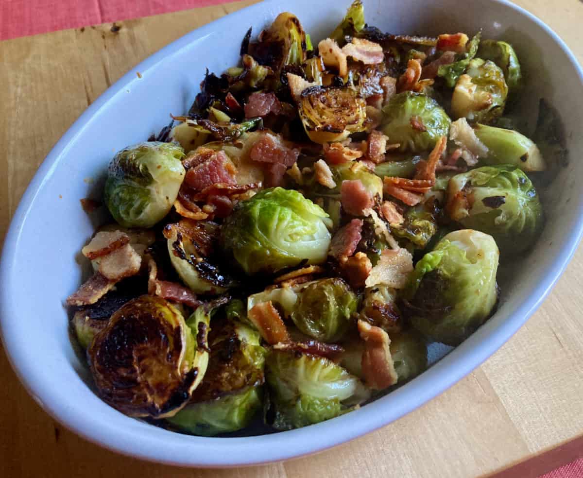 Skillet roasted brussels sprouts with bacon in oval white ceramic dish.