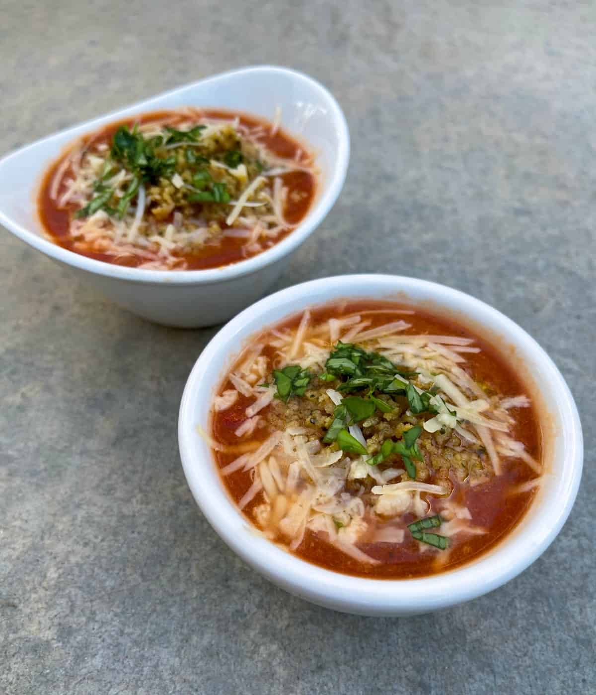 Two bowls of chicken parmesan soup on gray counter.