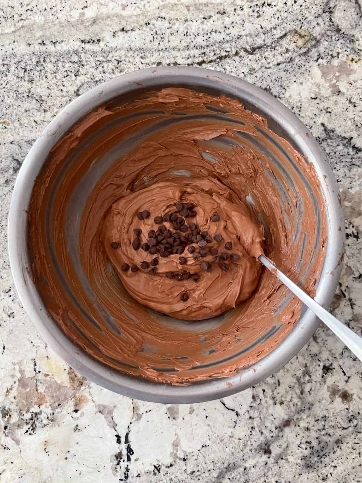 Stirring miniature chocolate chips into spoonable chocolate cheesecake mixture.