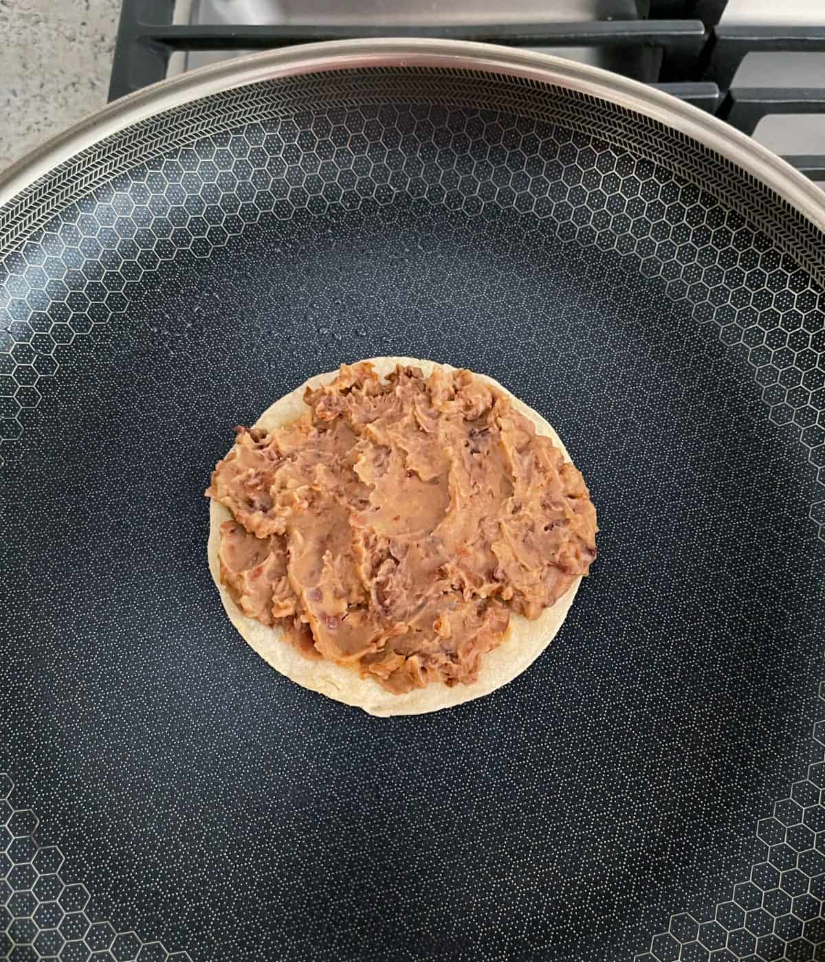 Heating tortilla spread with refried beans in skillet.