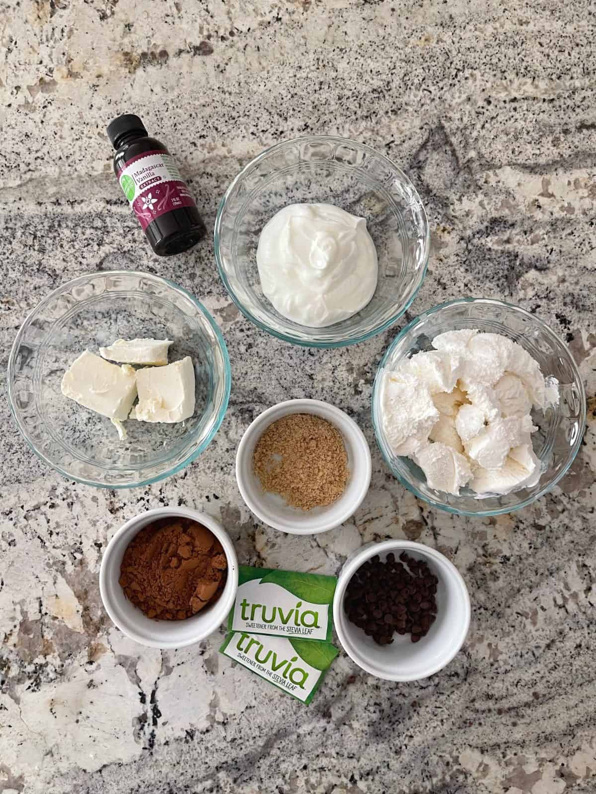 Ingredients including vanilla, Greek yogurt, light cream cheese (at room temperature), light whipped topping, graham cracker crumbs, cocoa powder, mini chocolate chips and zero calorie sweetener packets.
