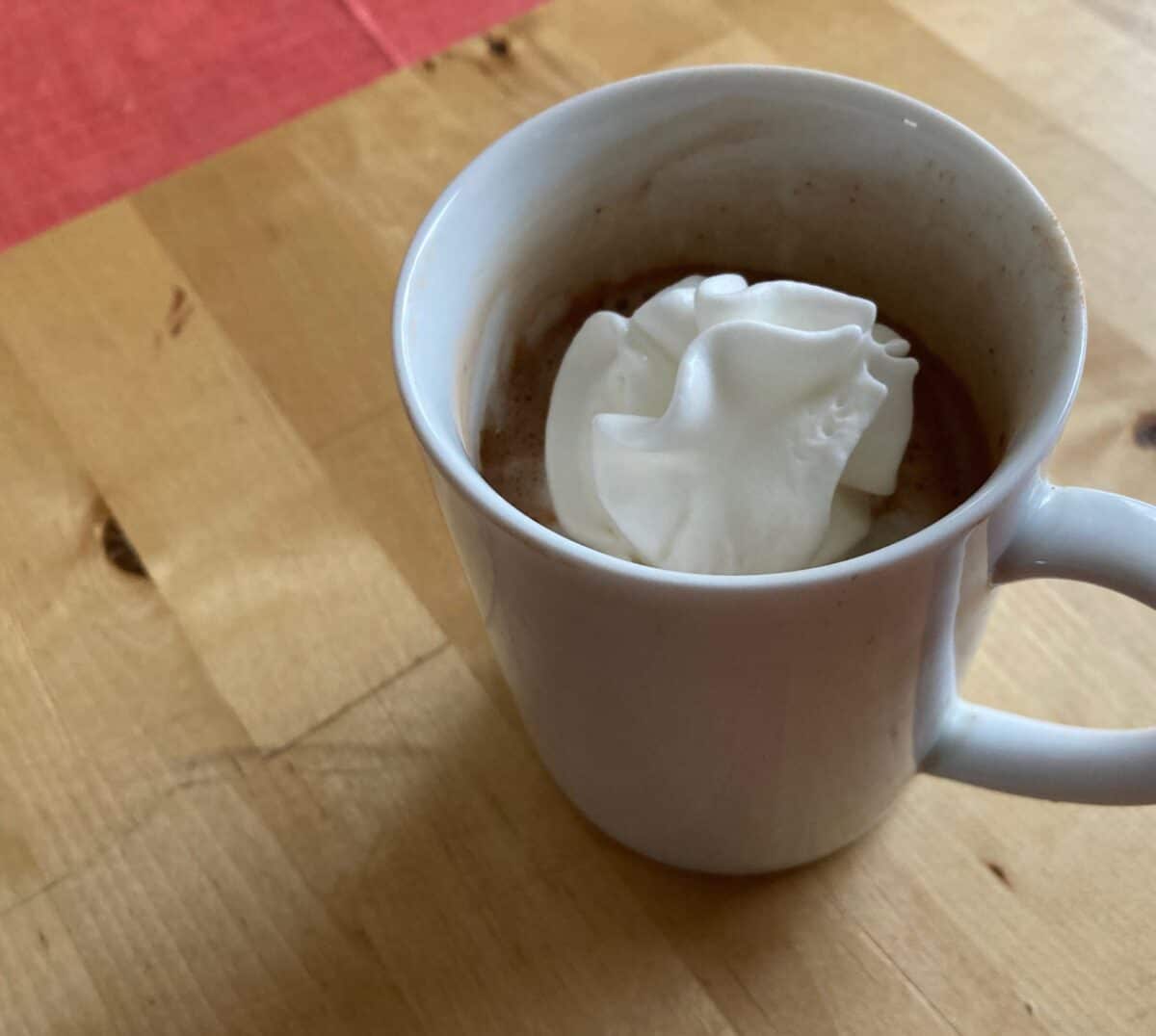 White mug of sugar-free hot chocolate with light whipped topping on butcher block.